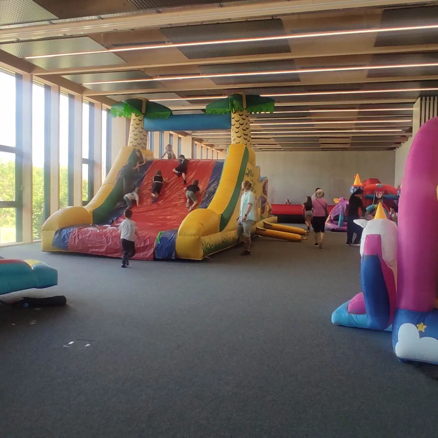 Salle de jeux intérieure colorée avec grand toboggan gonflable et structures décoratives, enfants qui jouent et parents supervisant.